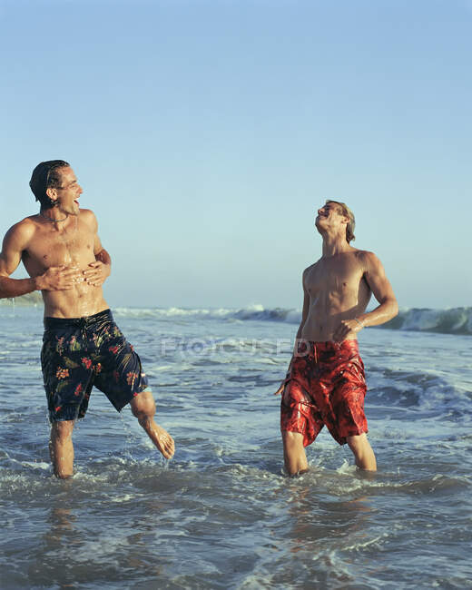 Hombres jugando en olas en la playa - foto de stock