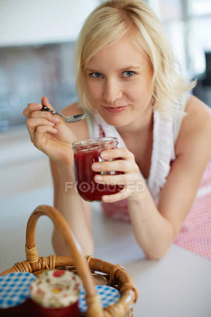 Mulher comendo geléia de jarro na cozinha — Fotografia de Stock