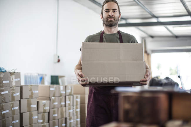 Portrait of man holding cardboard box in factory — Stock Photo