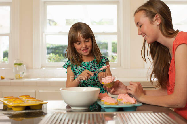 Young girl with older sister icing cupcakes — Stock Photo