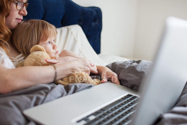 Mother and daughter lying in bed with laptop computer — Stock Photo