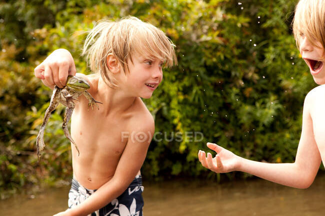 Boy holding frog up whilst friend looks on in amazement — Stock Photo