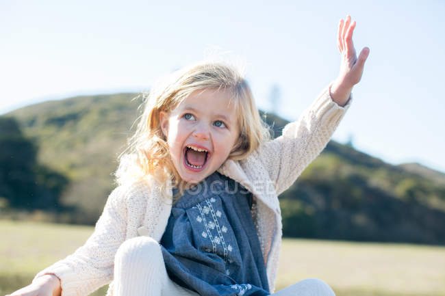 Cute blond girl sitting waving in field landscape — Stock Photo