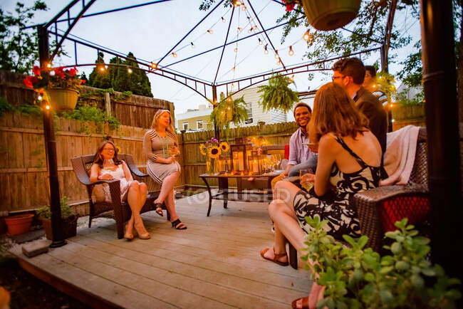 Група людей на вечірці в саду, сидить на палубі, розмовляє — стокове фото
