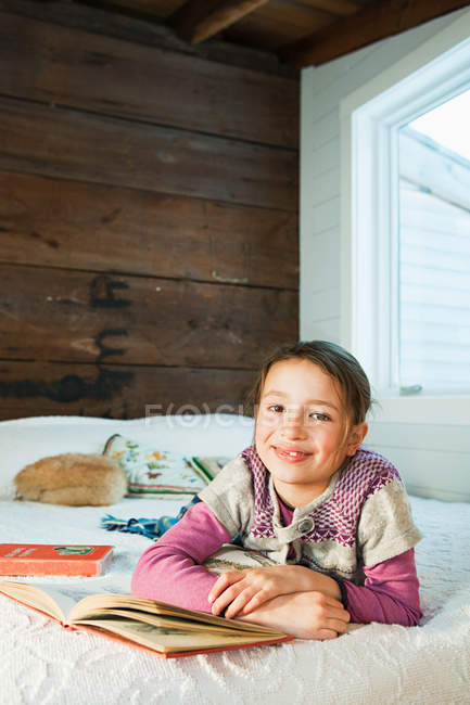 Young girl lying on bed reading book — Stock Photo