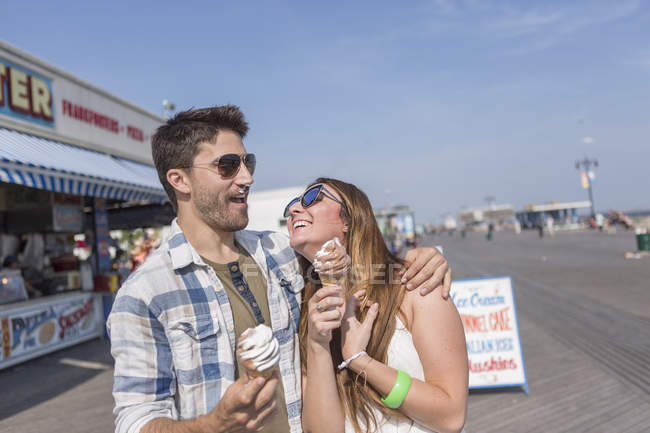 Pareja contemporánea pasar un buen rato en el paseo marítimo parque de atracciones comiendo helado suave - foto de stock