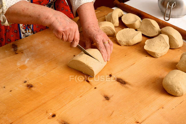Cropped image of senior woman slicing dough on cutting board — Stock Photo