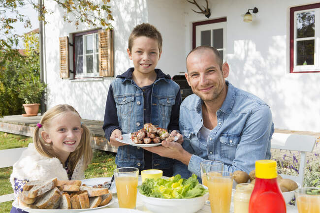 Portrait de père et d'enfants à la table de barbecue du jardin — Photo de stock