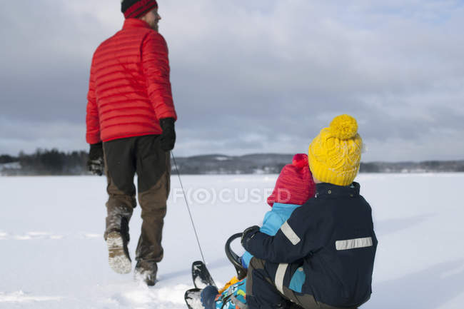 Батько тягне синів на санях у сніжному покритому ландшафті, вид ззаду — стокове фото