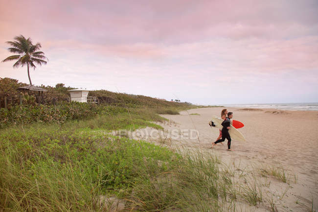 Salvavidas masculinas y surfista corriendo hacia el mar desde la playa. - foto de stock