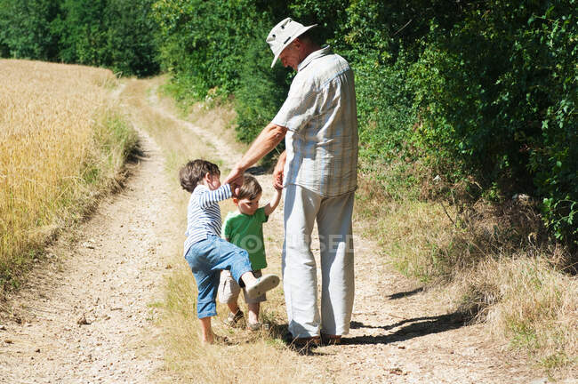 Дедушка и внуки идут по сельской дороге — стоковое фото