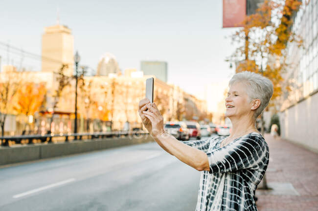 Mulher sênior ao ar livre, usando smartphone, sorrindo — Fotografia de Stock