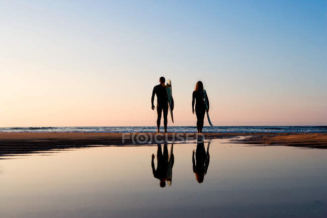 Вид ззаду пари, що стоїть на пляжі, відображення у воді — стокове фото