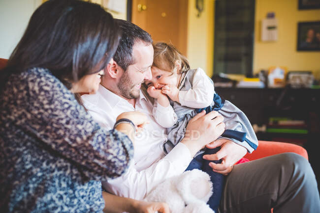 Shy female toddler sitting on fathers lap in living room — Stock Photo
