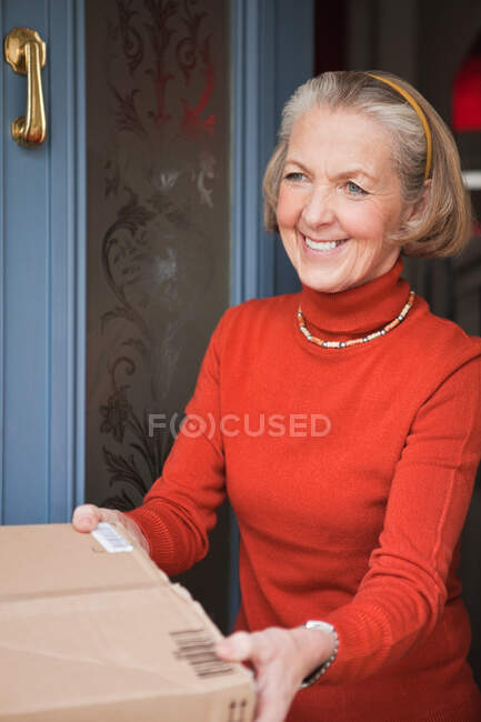Senior woman receiving parcel at front door — Stock Photo