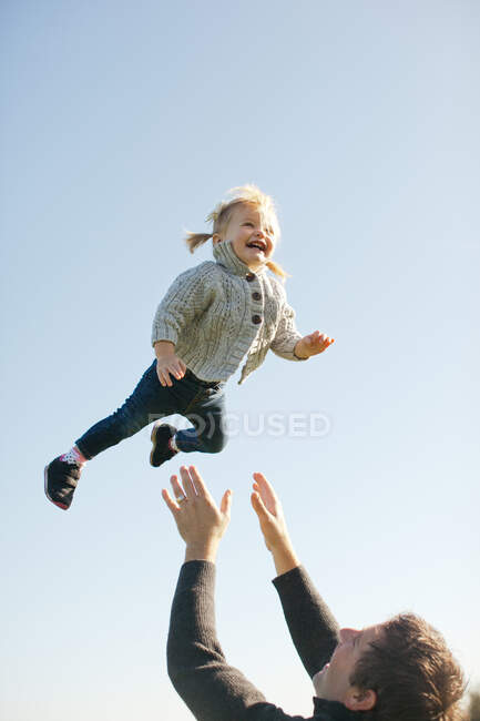 Femme tout-petit jeté en l'air par le père contre le ciel bleu — Photo de stock
