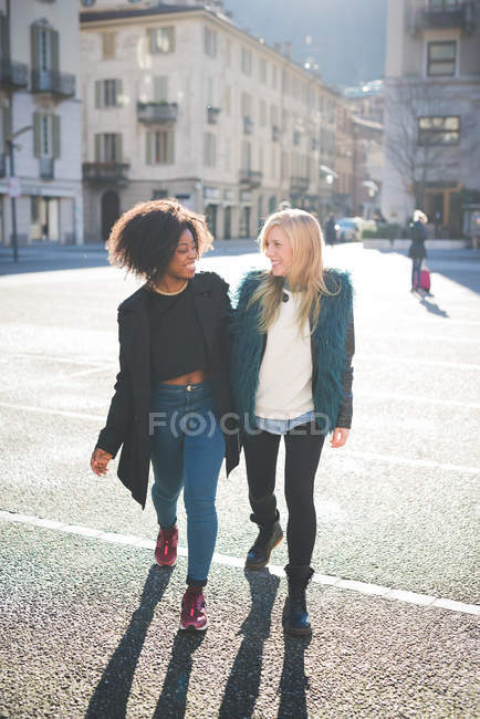 Two female friends talking and strolling in town square — Stock Photo