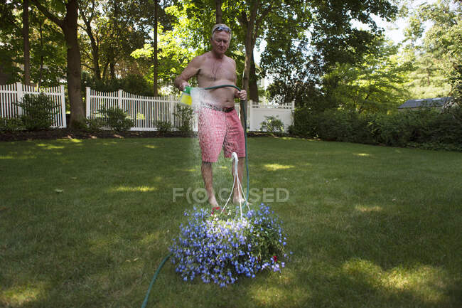Старший мужчина на заднем дворе поливает цветочный завод — стоковое фото