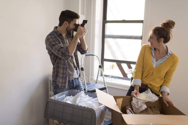 Feliz jovem casal se movendo no apartamento urbano se divertindo com a velha câmera — Fotografia de Stock