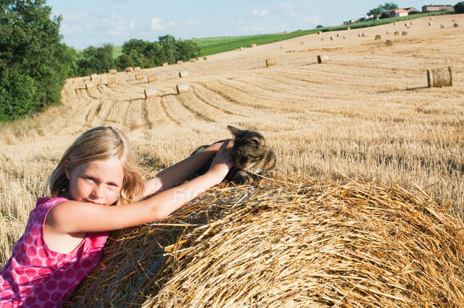 Menina com gato no fardo de feno no campo — Fotografia de Stock