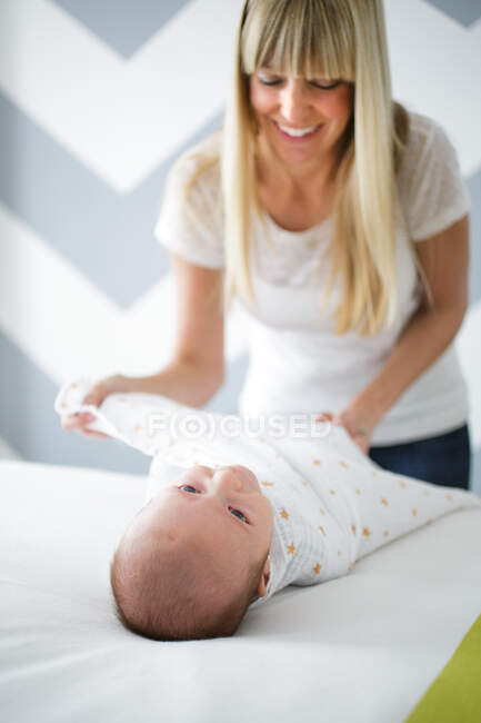 Femme adulte milieu emmaillotant bébé fils sur le lit — Photo de stock