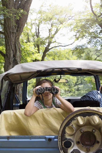 Menina olhando para fora do veículo off-road, usando binóculos — Fotografia de Stock