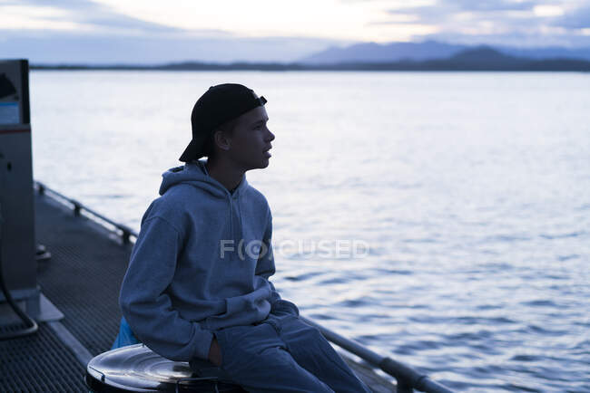 Adolescente sentado en el muelle mirando hacia otro lado, Pacific Rim National Park, Vancouver Island, Canadá - foto de stock
