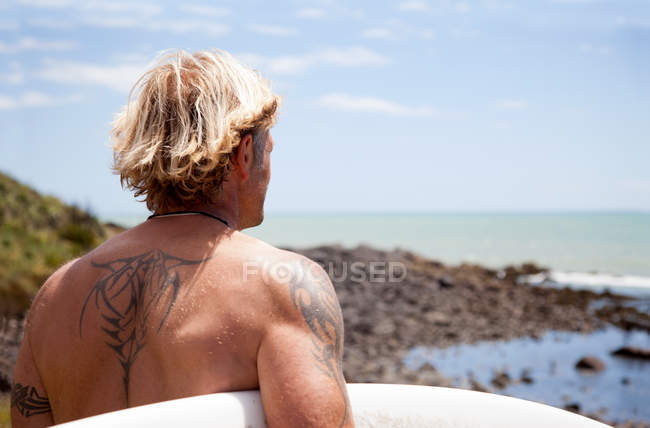 Rückansicht eines reifen Mannes mit Surfbrett am Strand — Stockfoto