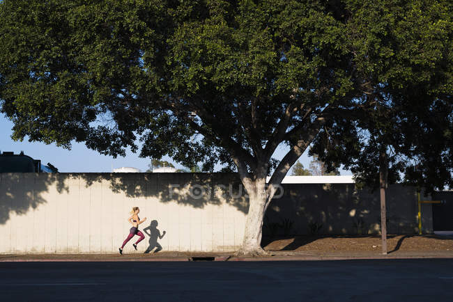 Jovem se exercitando ao ar livre, correndo ao longo da estrada — Fotografia de Stock