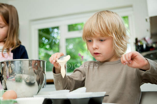Junge löffelt Kuchenmischung in Kuchentüten — Stockfoto