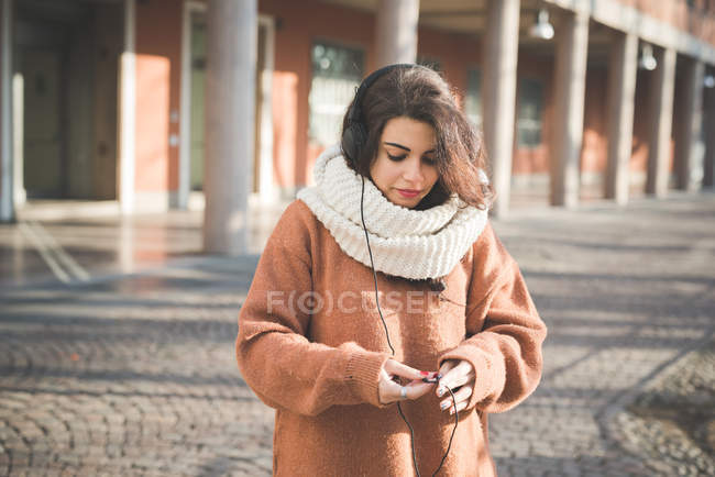 Mujer joven examinando cable auriculares en la calle - foto de stock