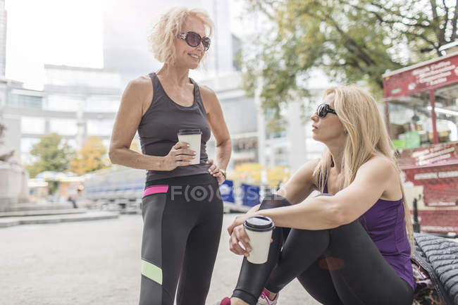 Duas amigas maduras treinando na cidade, conversando com o café takeaway — Fotografia de Stock