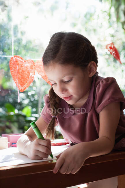 Дівчина сидить за віконним столом малює з креоном — стокове фото