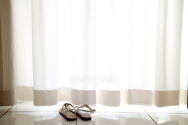 Par de sandalias en el suelo bajo la cortina - foto de stock
