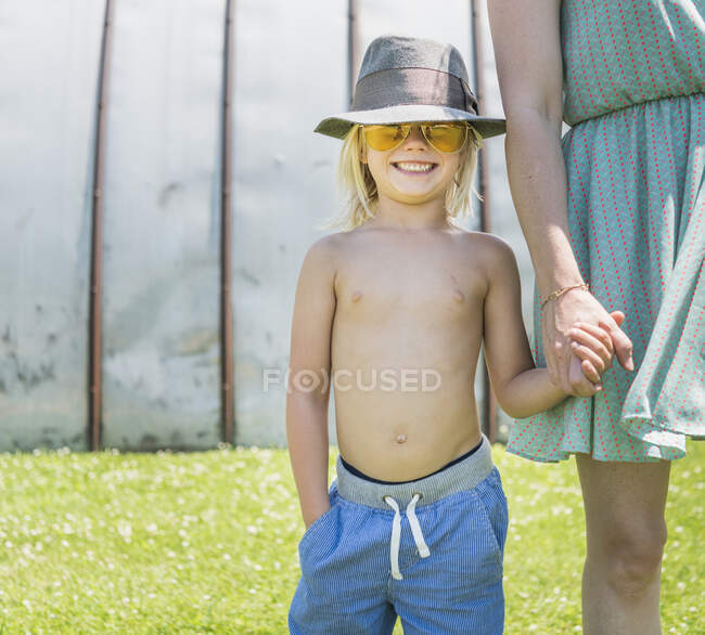 Junge mit Sonnenbrille und Hut hält Mutter an der Hand — Stockfoto