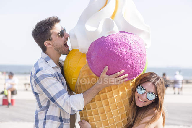 Contemporary couple having a good time on amusement park boardwalk with giant ice creme model — Stock Photo