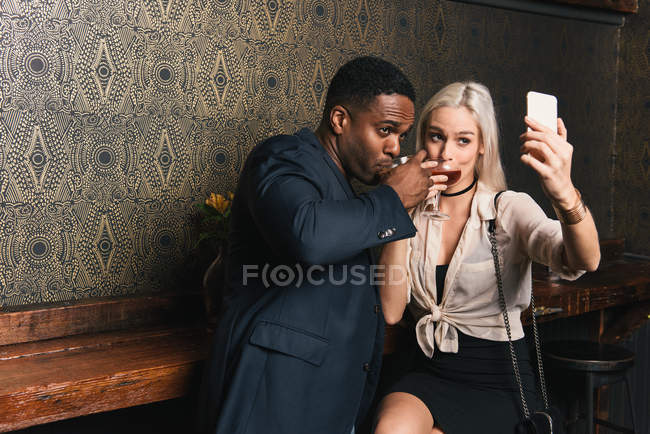 Pareja multicultural tomando selfie en pub - foto de stock