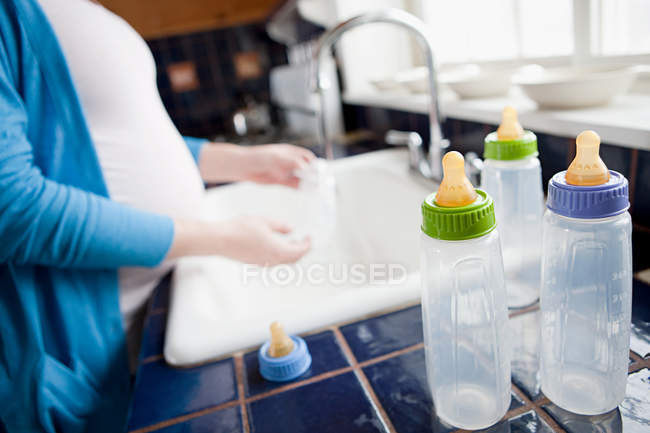 Беременная женщина стирает детские бутылочки — стоковое фото