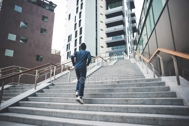 Vue arrière du jeune coureur masculin qui monte les escaliers de la ville — Photo de stock