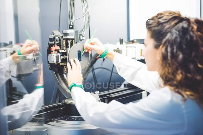 Жінка-вчена позиціонує зразок тонкої плівки на тримачі зразків на рентгенівському дифрактометрі — стокове фото