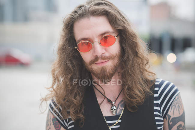 Portrait de jeune hippie mâle aux lunettes de soleil orange et aux cheveux longs — Photo de stock