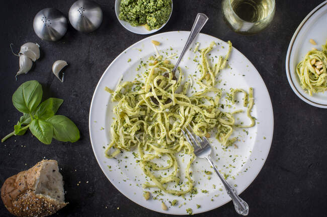A devoured plate of pesto pasta with ingredients surrounding plate and a glass of white wine, overhead view — Stock Photo