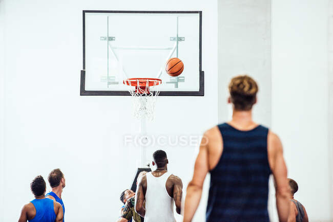 Vista trasera del equipo de baloncesto masculino viendo la pelota entrar en el aro en la cancha de baloncesto - foto de stock