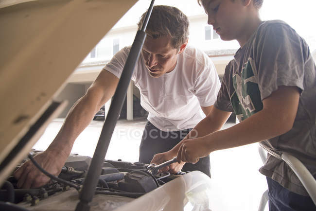 Padre mostrando hijo mantenimiento del coche bajo la campana del coche - foto de stock