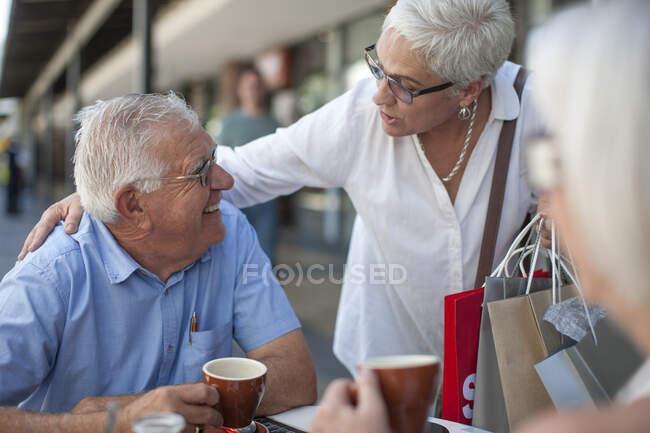 Ciudad del Cabo Sudáfrica, mujer anciana charlando con el hombre en el restraunt con sus bolsas de compras mientras toma un café - foto de stock