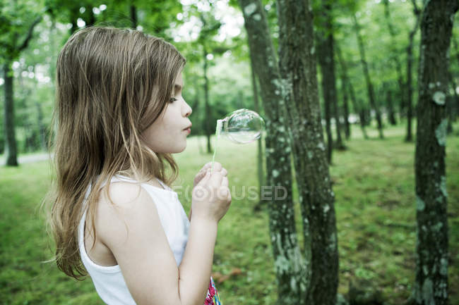 Fille souffler des bulles dans la forêt — Photo de stock
