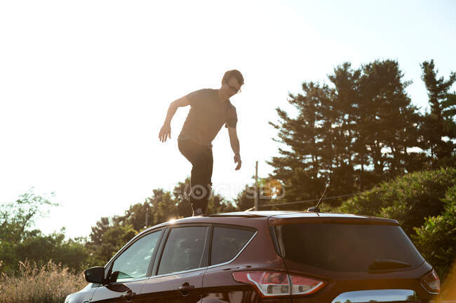 Giovane uomo che cammina sul tetto dell'auto — Foto stock