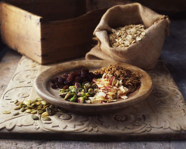 Dried fruits and nuts on wooden plate with burlap sack of oats — Stock Photo