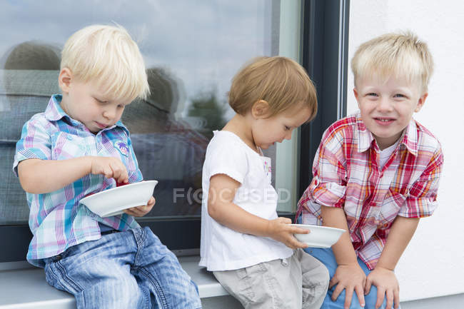 Criança feminina e dois irmãos jovens no pátio comendo framboesas — Fotografia de Stock