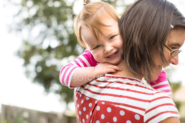 Mutter trägt kleine Tochter im Freien, lächelt — Stockfoto